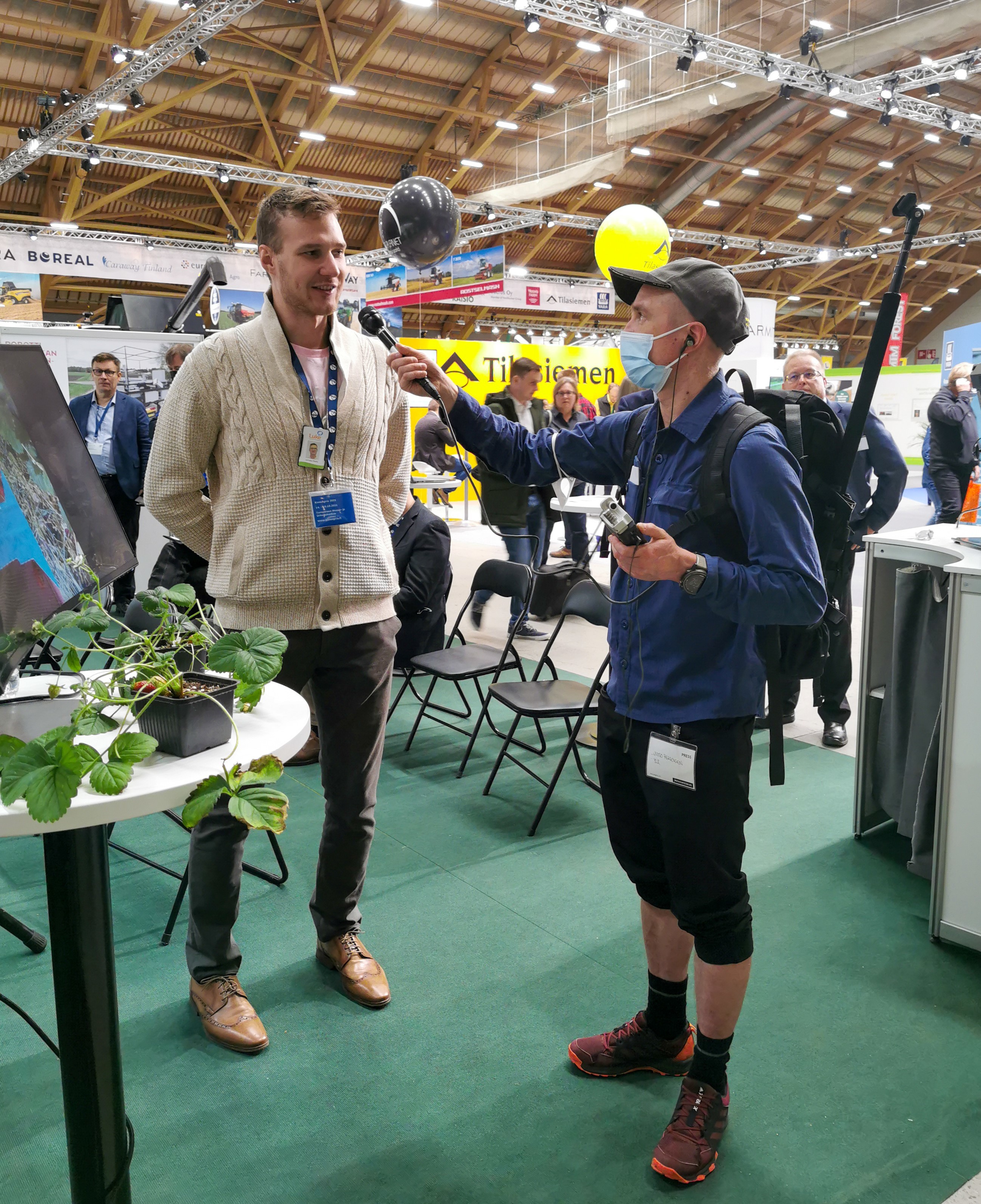 Kuvassa Madis Lemsalu Luonnonvarakeskuksesta esittelee mansikanpoimintarobottia Ylen toimittaja Juuso Pekkiselle.