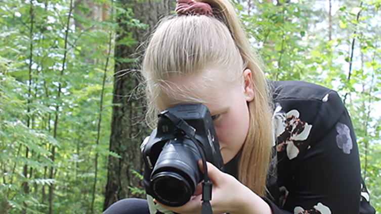 Tyttö kuvaa kameralla metsässä