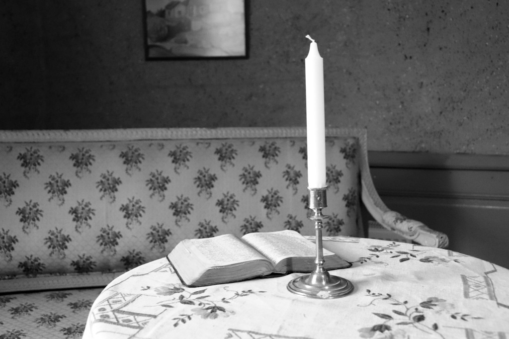 Mustavalkoinen kuva sohvasta sekä pöydästä, jossa on kynttilä ja avonainen kirja.